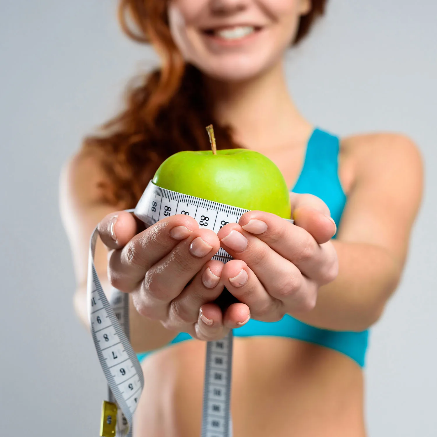 Eine Frau in sportlicher Kleidung präsentiert vor der Kamera einen Apfel, der mit einem Maßband umwickelt ist.