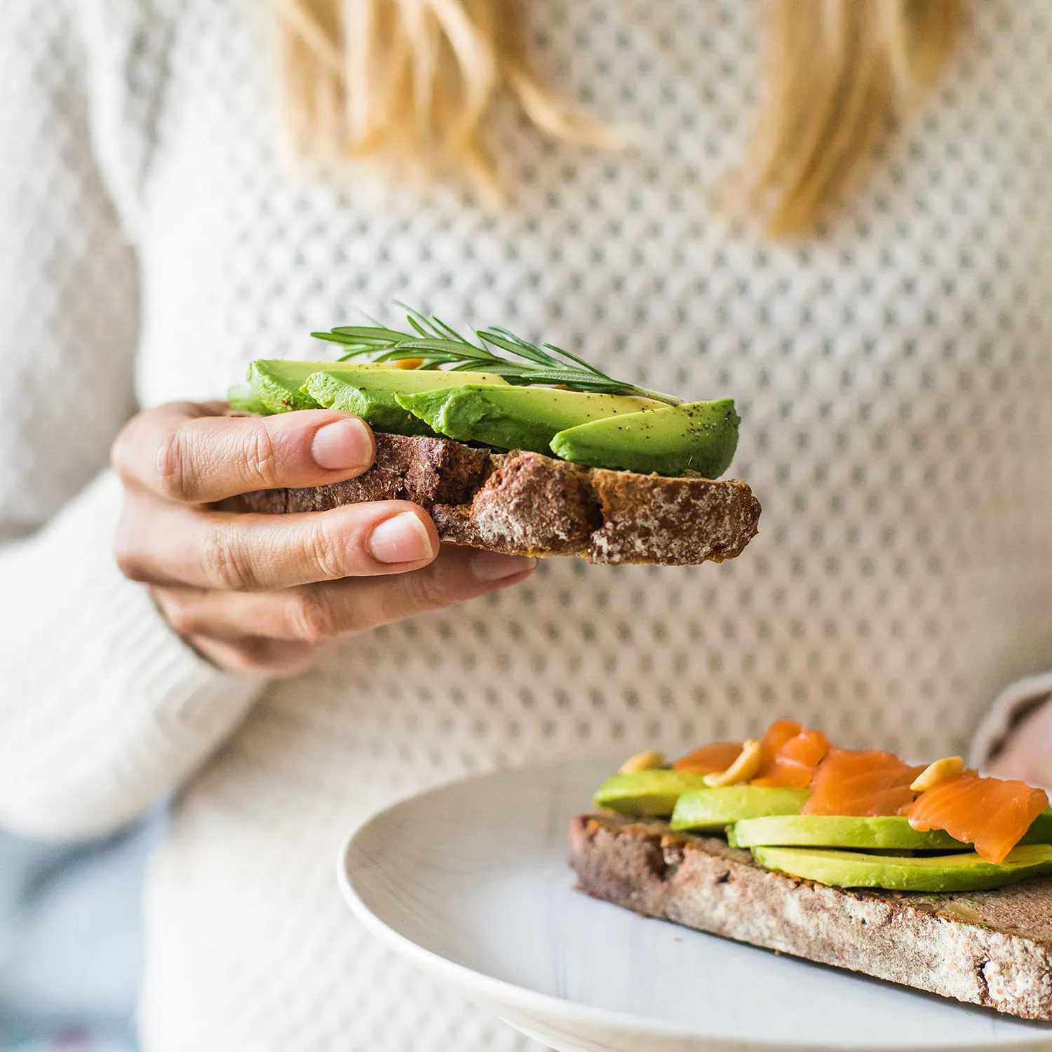 Eine Person die ein frisches Avocadobrot in die Kamera hält.